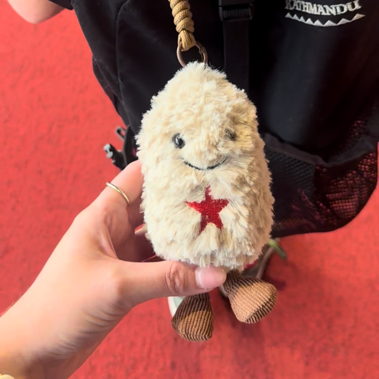 Small peanut plush toy with a red star held by a hand against a red background.