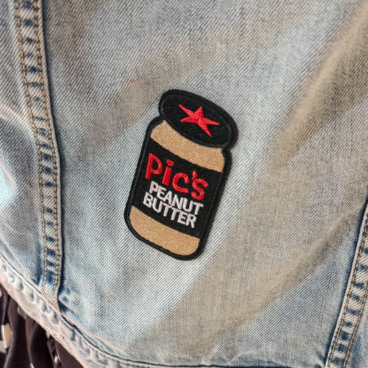 Person wearing a denim jacket with a 'Pic's Peanut Butter' patch on a red background