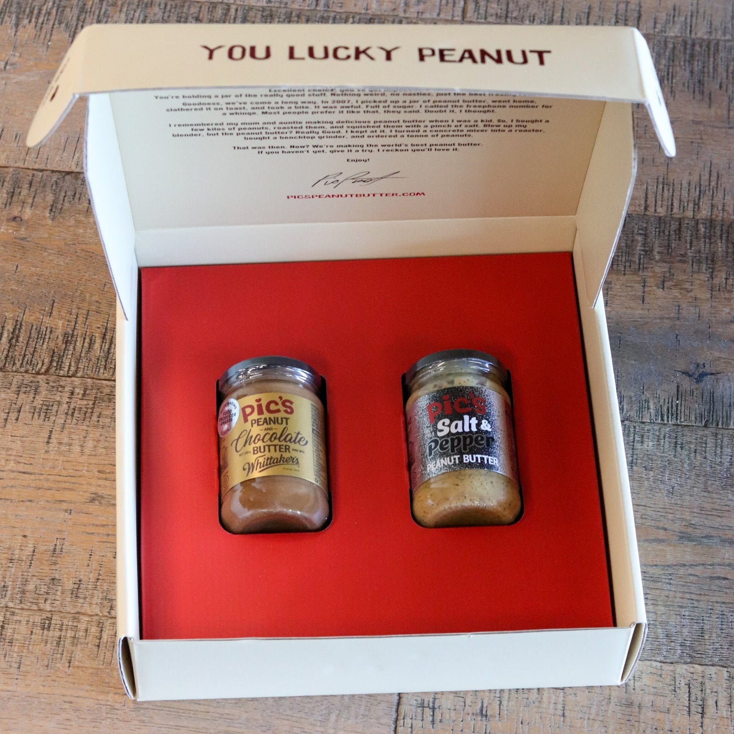 Two jars of pickle relish in a box labeled 'You Lucky Peanut' on a wooden surface.